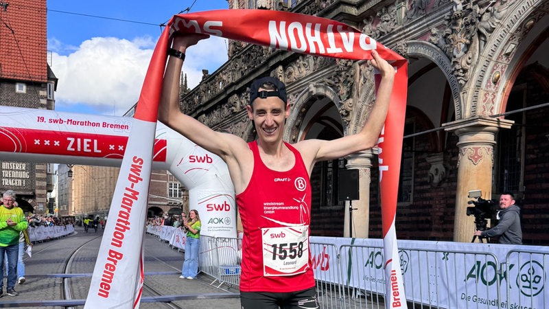 Der Sieger des Bremen-Marathon, Leonard Maisch, reckt im Ziel strahlend das rot-weiße Band in die Höhe.