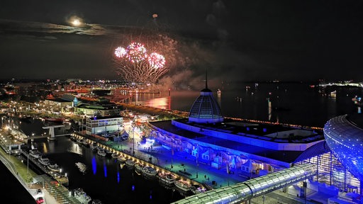 Blick von oben auf das Hafengelände in Bremerhaven. Am Himmel ist ein Feuerwerk zu sehen.