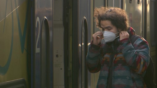 Ein Fahrgast setzt seine Maske auf während er in den Zug steigt.