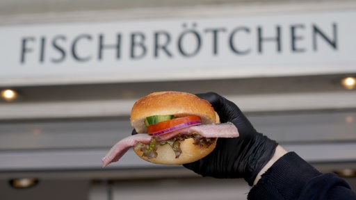 Ein Matjes Fischbrötchen wird vor einem Schild gehalten