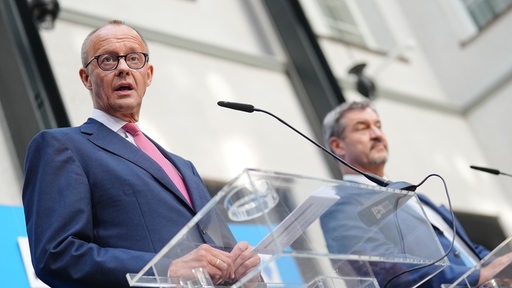 Merz und Söder stehen vor einem Rednerpult bei einer Pressekonferenz.