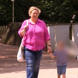 Eine junge Frau mit blonden Haaren geht einen Weg entlang und hält ein Kind an der Hand