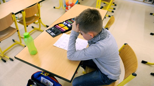 Ein Schüler sitzt in einem leeren Klassenzimmer nach (Symbolbild)