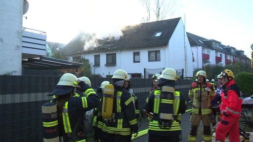 Feuerwehrmänner stehen vor einem Reihenhaus, in dem es eine Explosion gab.