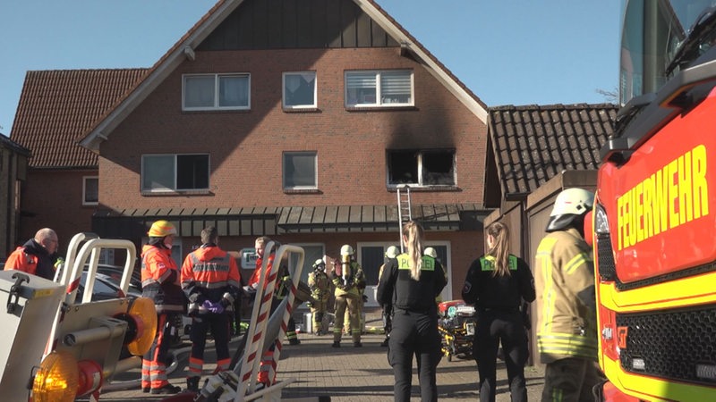 Feuerwehrleute und Polizisten stehen vor einem roten Backsteinhaus.