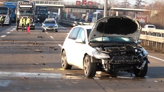 Ein zerstörtes Auto steht auf einer Autobahn. Im Hintergrund sind Polizisten zu sehen.