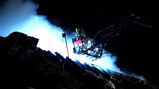 Feuerwehrleute löschen von einem Leiterfahrzeug aus einen Brand in einem Gebäude.