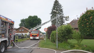 Feuerwehrleute löschen von einer Drehleiter aus ein Feuer in einem Einfamilienhaus mit Löschschaum.