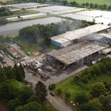 Eine ausgebrannte Halle aus der Luft fotografiert. Qualm ist zu sehen.