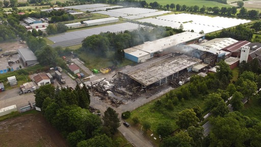 Eine ausgebrannte Halle aus der Luft fotografiert. Qualm ist zu sehen.