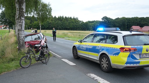 Ein E-Bike steht neben einem Auto, das gegen einen Baum gefahren ist.