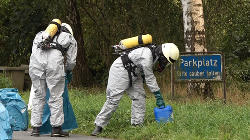 Menschen in Schutzanzügen packen Kanister in Plastiksäcke.