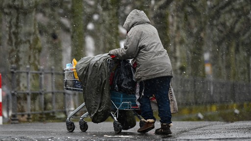 Eine obdachlosen Frau schiebt bei Schneefall ihr Hab und Gut in einem Einkaufswagen