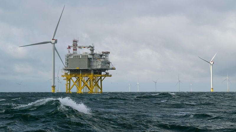 Eine Welle schwappt vor einer Offshore-Windkraftanlage, die in der Nordsee aufgebaut ist.