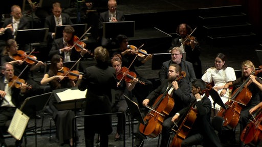 Zwei Gäste sitzen zwischen Orchester Musikern