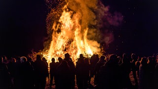 Menschen stehen um ein Osterfeuer herum.