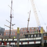 Ein Kran hebt einen Mast eines Schiffes in die Höhe