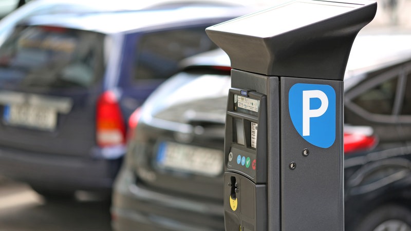 Autos parken hinter einem Parkscheinautomaten.