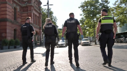 Vier Polizisten gehen eine Straße entlang.