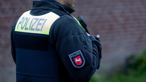 Ein Beamter der Polizei Niedersachsen in Polizeiuniform und mit dem Landeswappen auf dem Arm.