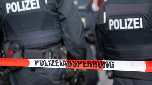 Polizisten stehen hinter einem Polizei-Flatterband.