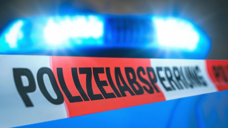 Eine Polizeiabsperrung führt vor einem Blaulicht entlang.