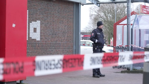 Ein Polizist steht hinter einem Absperrband.