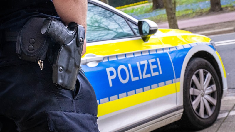 Ein Polizist im Einsatz, Einsatzfahrzeug im Hintergrund, Waffe im Gürtel