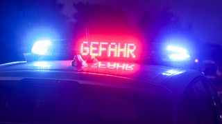 Mit Blaulicht und der Anzeige "Gefahr" steht ein Polizeifahrzeug auf der Autobahn.