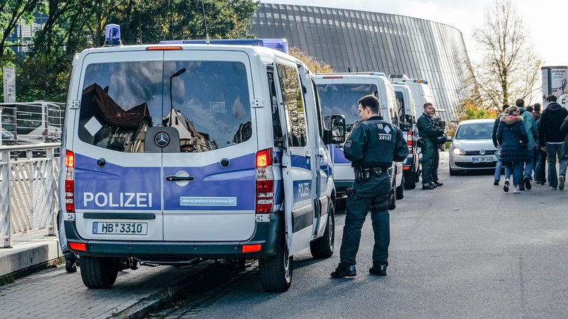 Einige Polizeiautos stehen in Reihe, ein Polizist steht daneben