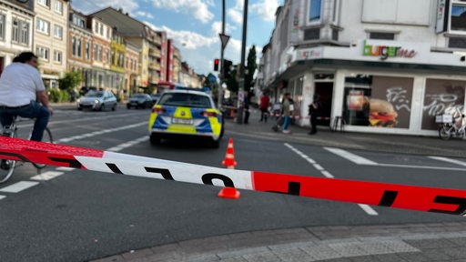 Ein Absperrband der Polizei, im Hintergrund ein Streifenwagen