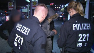 Zwei Polizisten bei einer Kontrolle an einer Haltestelle.