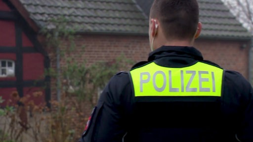 Ein Polizist ist von hinten zu sehen. Er seht vor einem Haus in Fischerhude.