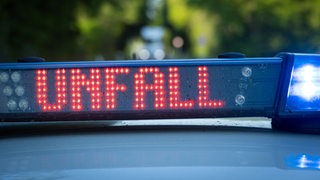 Ein Einsatzfahrzeug der Polizei steht mit Blaulicht und dem Schriftzug Unfall im Display an einem Unfallort.