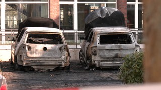 Vor einer Polizeiwache stehen zwei ausgebrannte Zivilfahrzeuge.