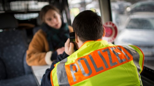 Ein Polizeibeamter überprüft die Personalien einer Frau in einem Polizeifahrzeug (Symbolbild)