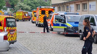 Zahlreiche Krankenwagen und Polizeiautos stehen hinter einer Absperrung.