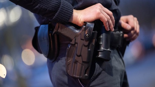 Die Hand eines Polizisten liegt auf seiner Waffe, die im Holster steckt.