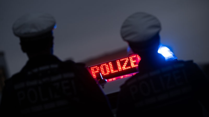 Zwei Polizisten stehen vor einem Polizeifahrzeug