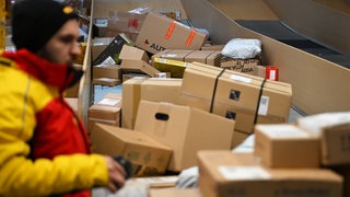 Ein Paketbote holt in einer Zustellbasis von DHL Pakete von einer Rutsche, um sie in seinen Transporter zu laden und seine Zustelltour zu beginnen.