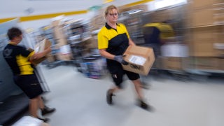 Eine Paketzustellerin sortiert im Laufschritt Pakete in einem Zustellstützpunkt der Deutschen Post. Bewegungsunscharfe Aufnahme