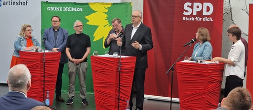 Mehrere Politiker stehen bei einer Pressekonferenz auf einem Podium.