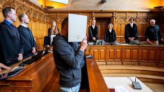 Zwei Angeklagte stehen vor ihren Anwälten im Gerichtsaal. 