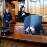 Eine Angeklagte sitzt vor Prozessbeginn im Gerichtssaal, vor ihrem Gesicht hält sie eine Akte.