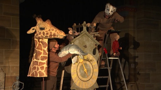 Menschen, als Tiere verkleidet und Handpuppen auf einer Bühne.