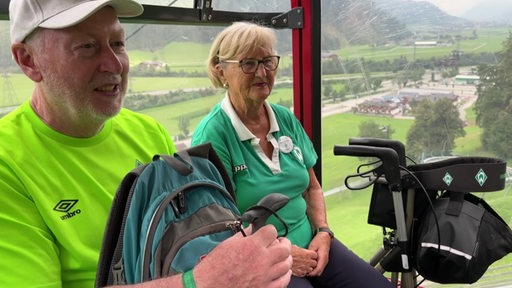 Zwei Senioren sitzen mit Werder-Bremen Kleidung in einer Seilbahn im Zillertal.