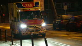 Ein Rettungswagen fährt im Dunkeln auf einer Straße.