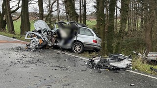 Nach einem Unfall liegt ein stark beschädigtes Auto neben der Straße. 