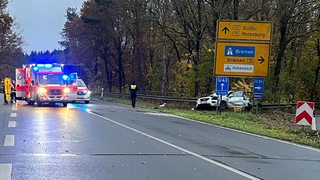 Auf einer Autobahn stehen mehrere Rettungswagen mit Blaulicht neben einem Auto, das in eine Leitplanke gefahren ist.