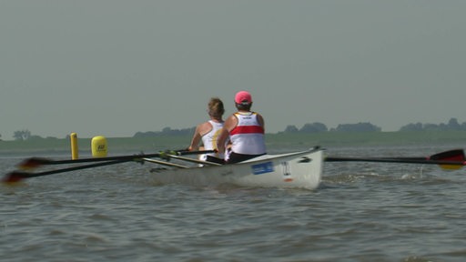 Zu sehen ist ein Ruderboot mit zwei Menschen darauf im Wasser.